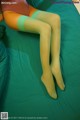 A woman in a pink bodysuit and green stockings laying on a bed.