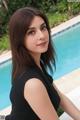 A woman in a black dress sitting by a swimming pool.