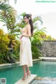 A woman in a white dress standing next to a pool.