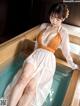 A woman in a white and orange dress sitting in a bathtub.