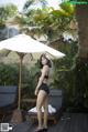 A woman in a black bathing suit standing under an umbrella.