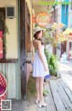 A woman in a white dress and hat standing on a porch.