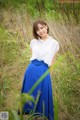 A woman in a white shirt and blue skirt standing in tall grass.