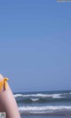 A woman in a yellow bikini standing on the beach.