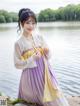 A woman in a purple and yellow hanbok sitting by the water.