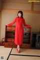 A woman in a red dress standing in front of a dresser.