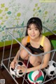 A young woman sitting on the floor with three soccer balls.