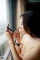 A naked woman applying makeup in front of a window.